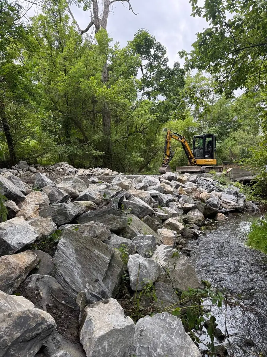 Shenk Excavation mini excavator placing stone riprap along a creek bank